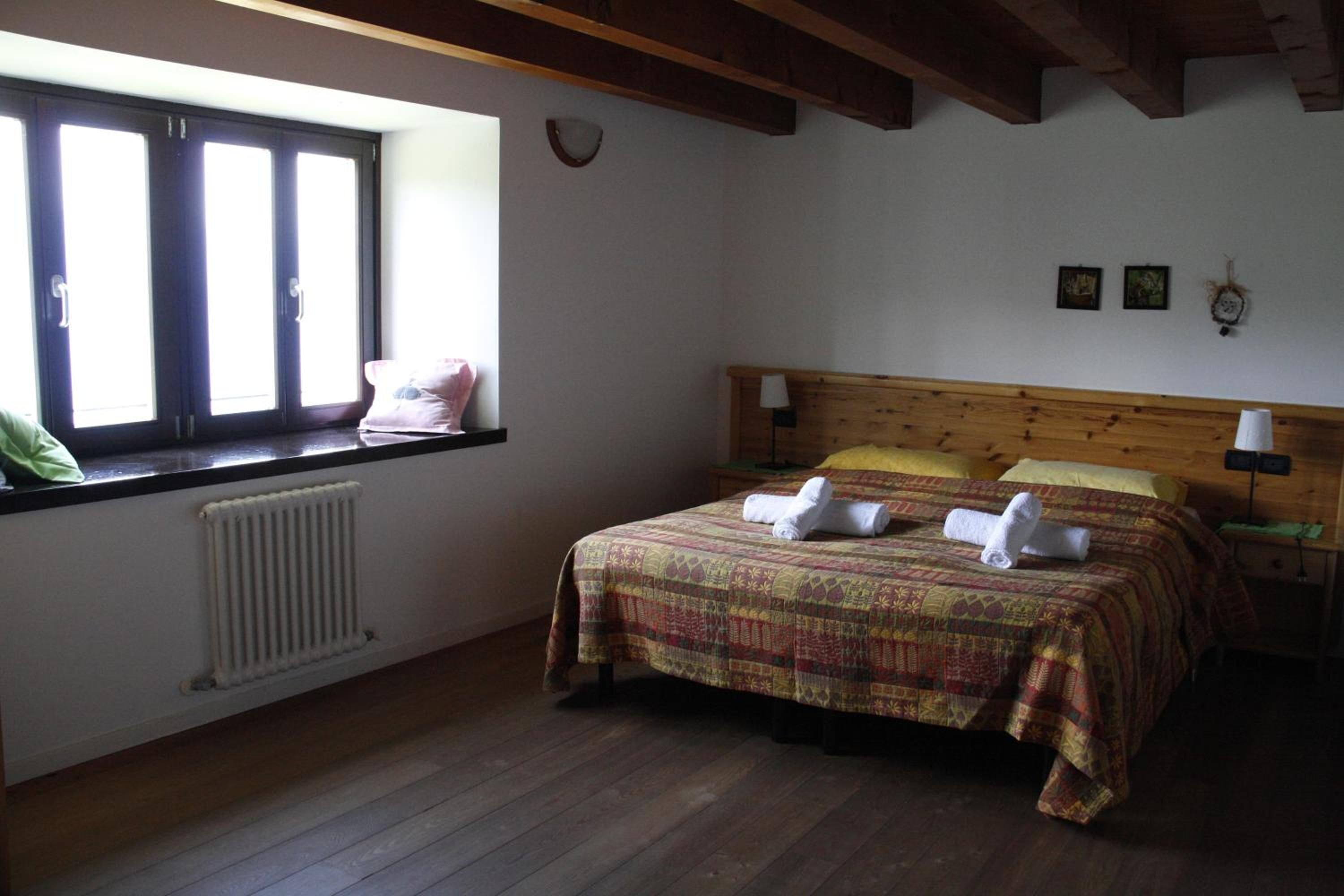 A bedroom with a wooden headboard, a radiator, a window with blinds, and a bed with a patterned bedspread and two pillows.