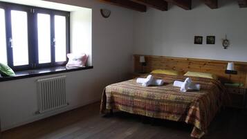 A bedroom with a wooden headboard, a radiator, a window with blinds, and a bed with a patterned bedspread and two pillows.
