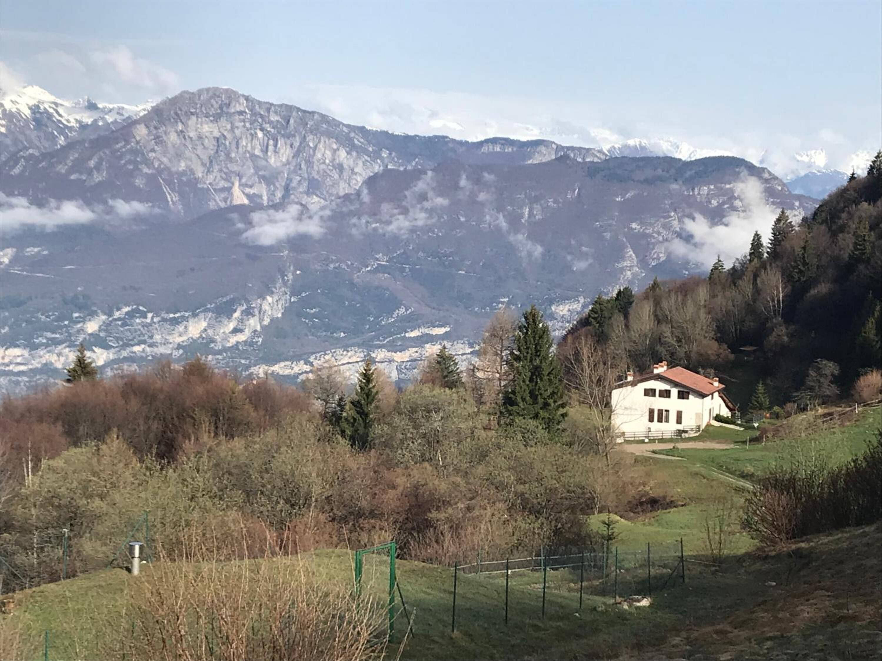 A white house with a red roof surrounded by a fenced yard, set against a backdrop of mountains and trees.