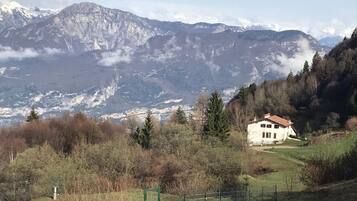 A white house with a red roof surrounded by a fenced yard, set against a backdrop of mountains and trees.