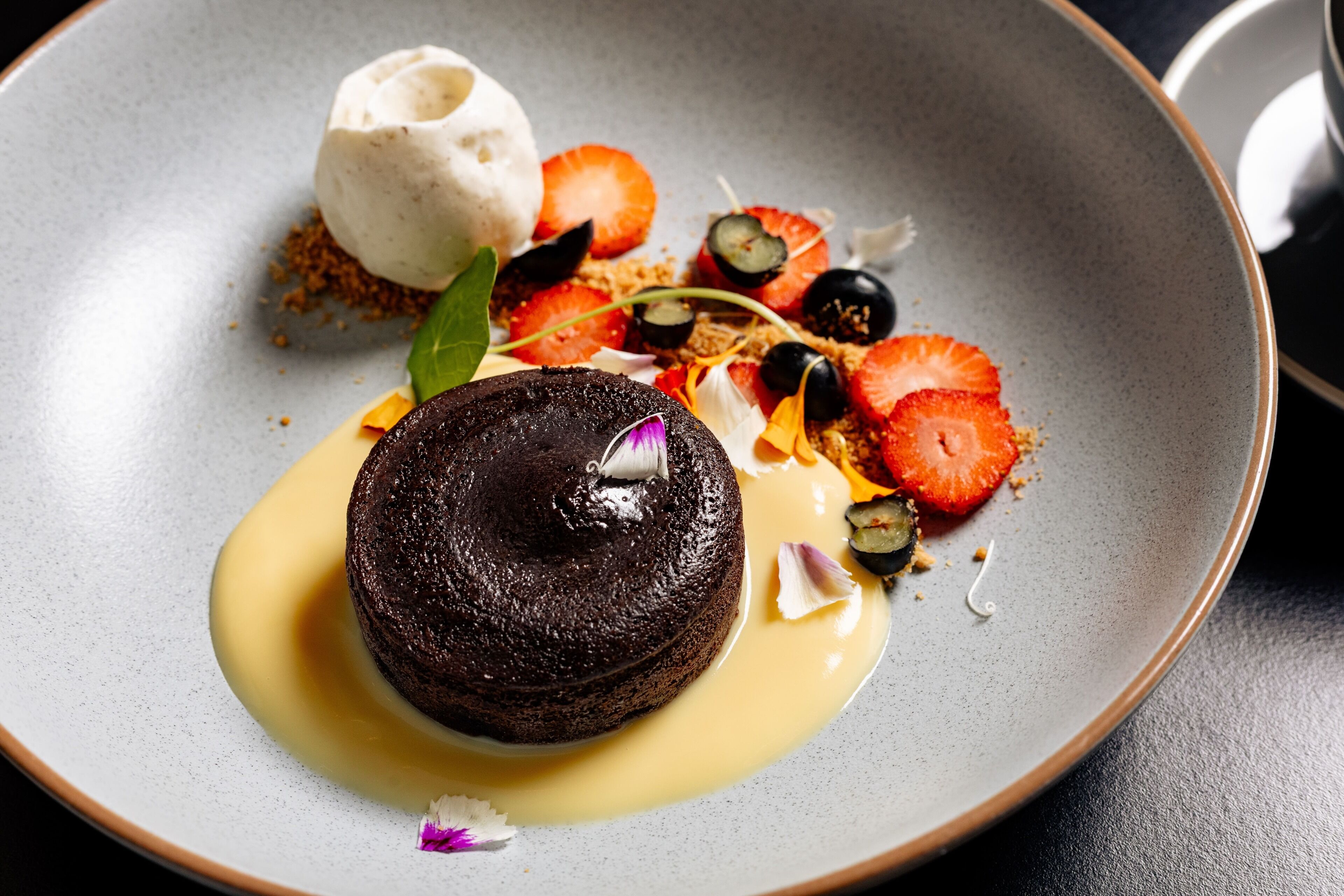 A dessert plate with a chocolate lava cake, ice cream, strawberries, and various garnishes.
