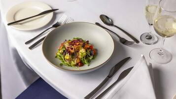 A dining table with a bowl of salad, cutlery, and glasses of white wine.