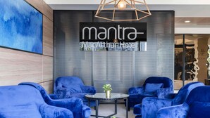 Un moderno vestíbulo de hotel con sillones azules, una mesa de centro negra y una pared grande con el nombre del hotel.