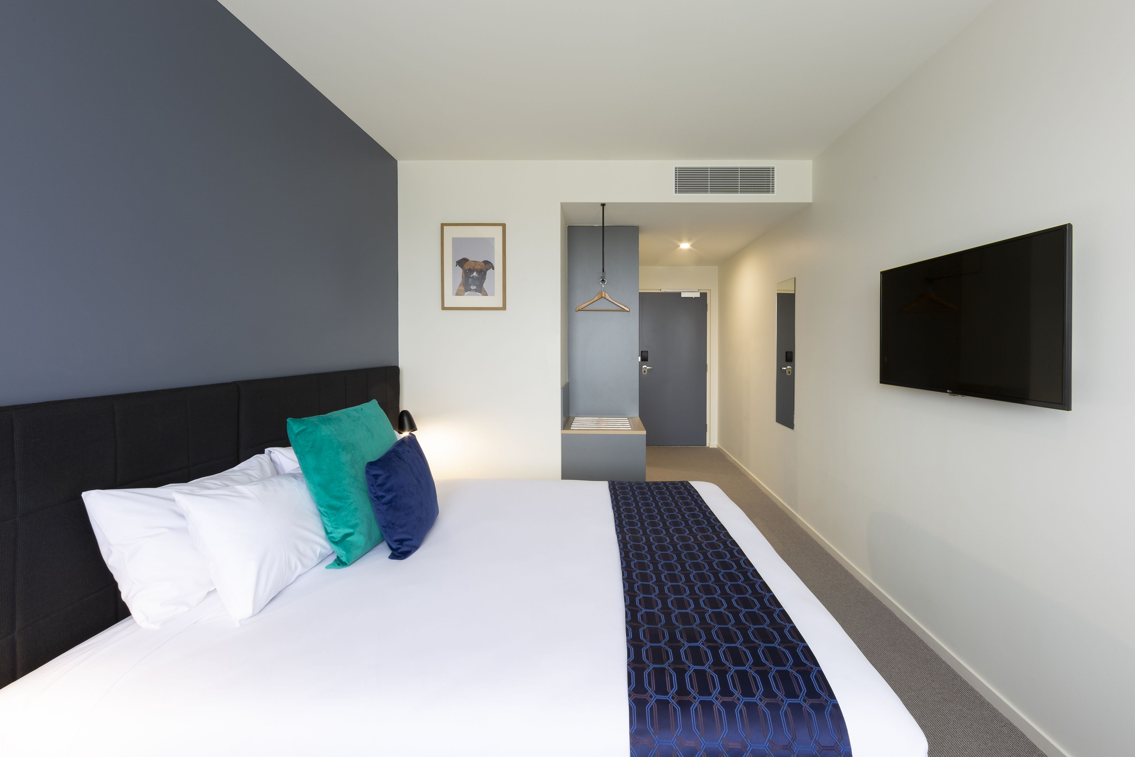 Habitación de hotel con una cama grande, un televisor montado en la pared y un cuadro enmarcado.