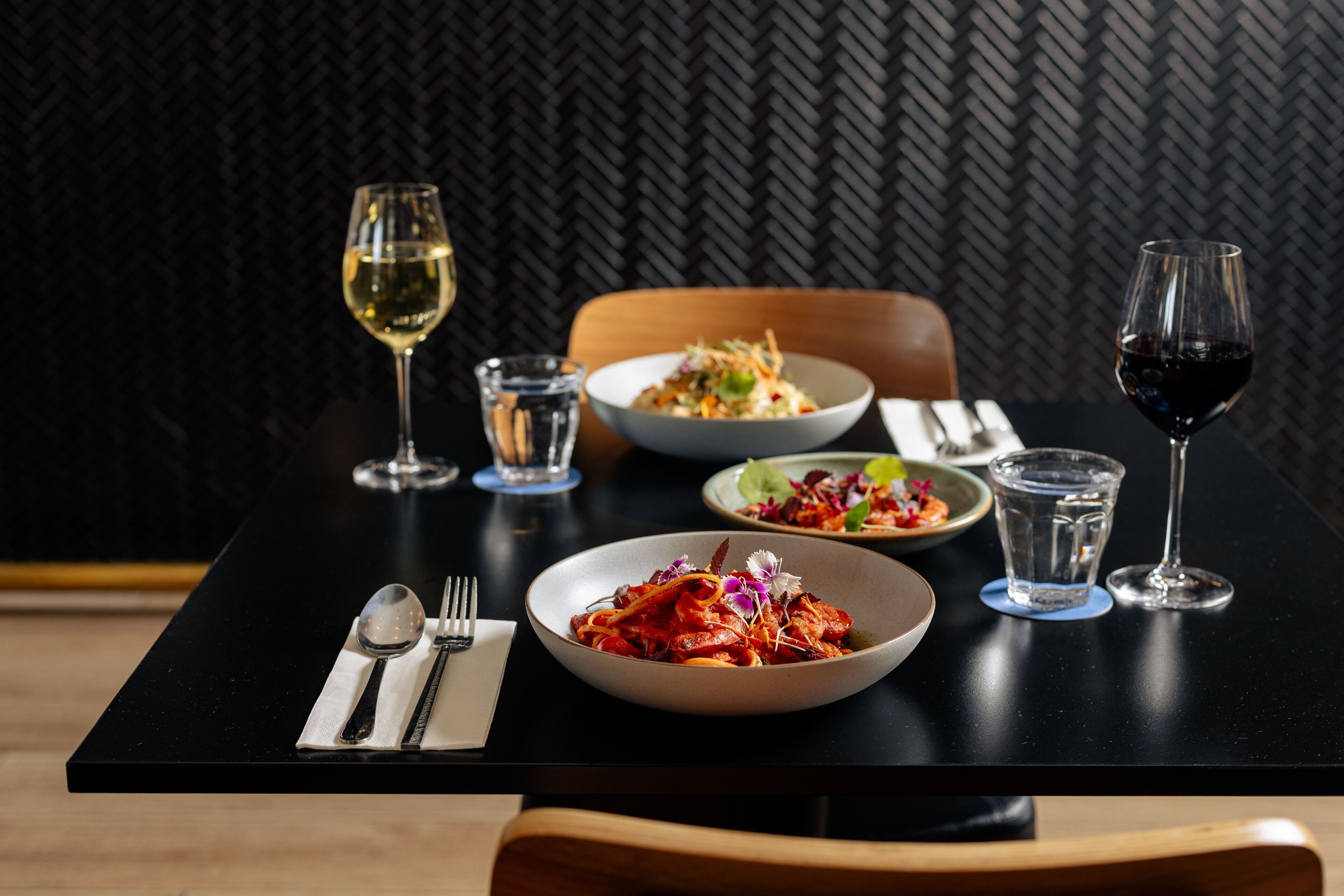 Une table à manger avec deux bols de nourriture, deux verres de vin et un verre d’eau.