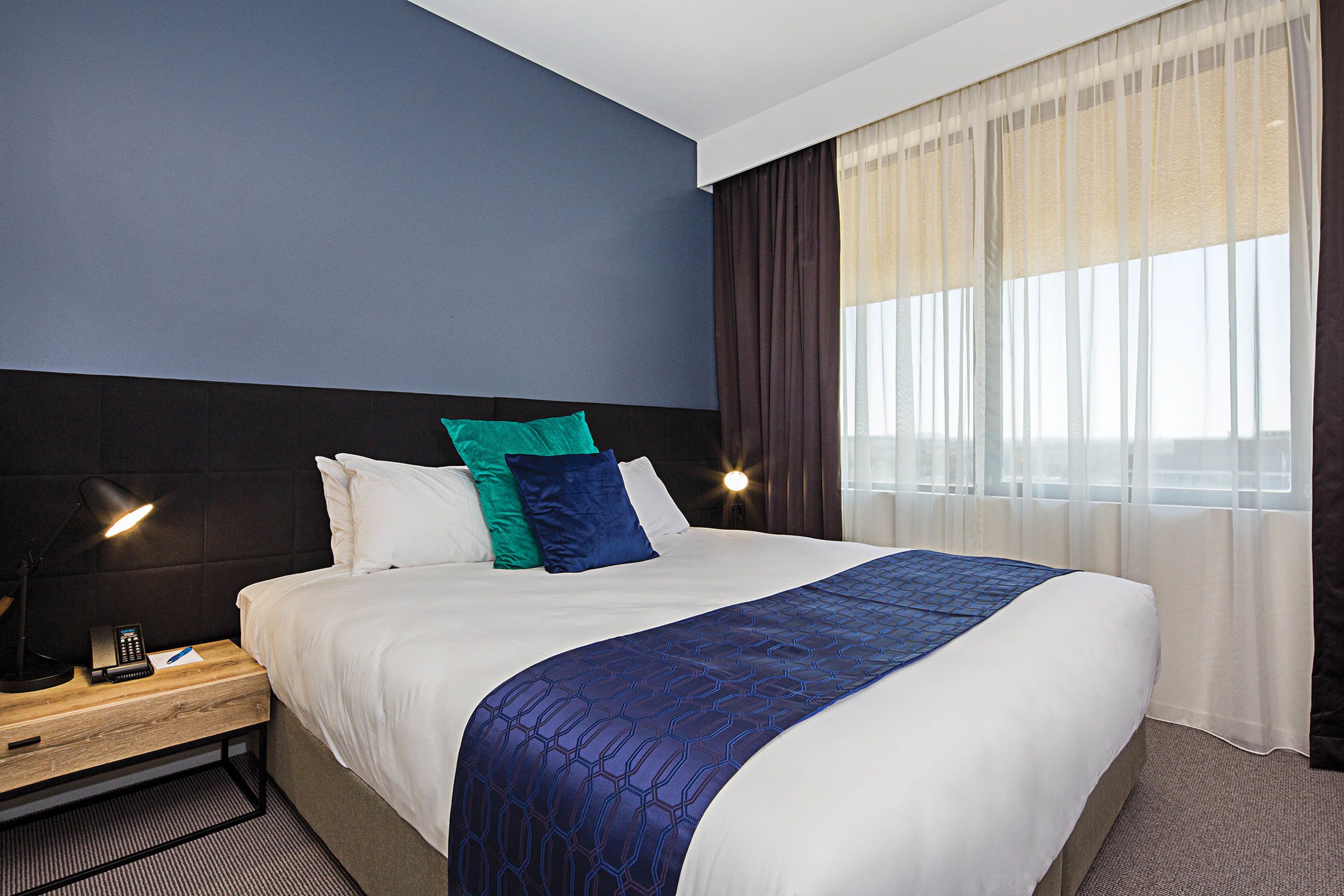 A hotel room with a large bed, a nightstand with a lamp, and a window with curtains.