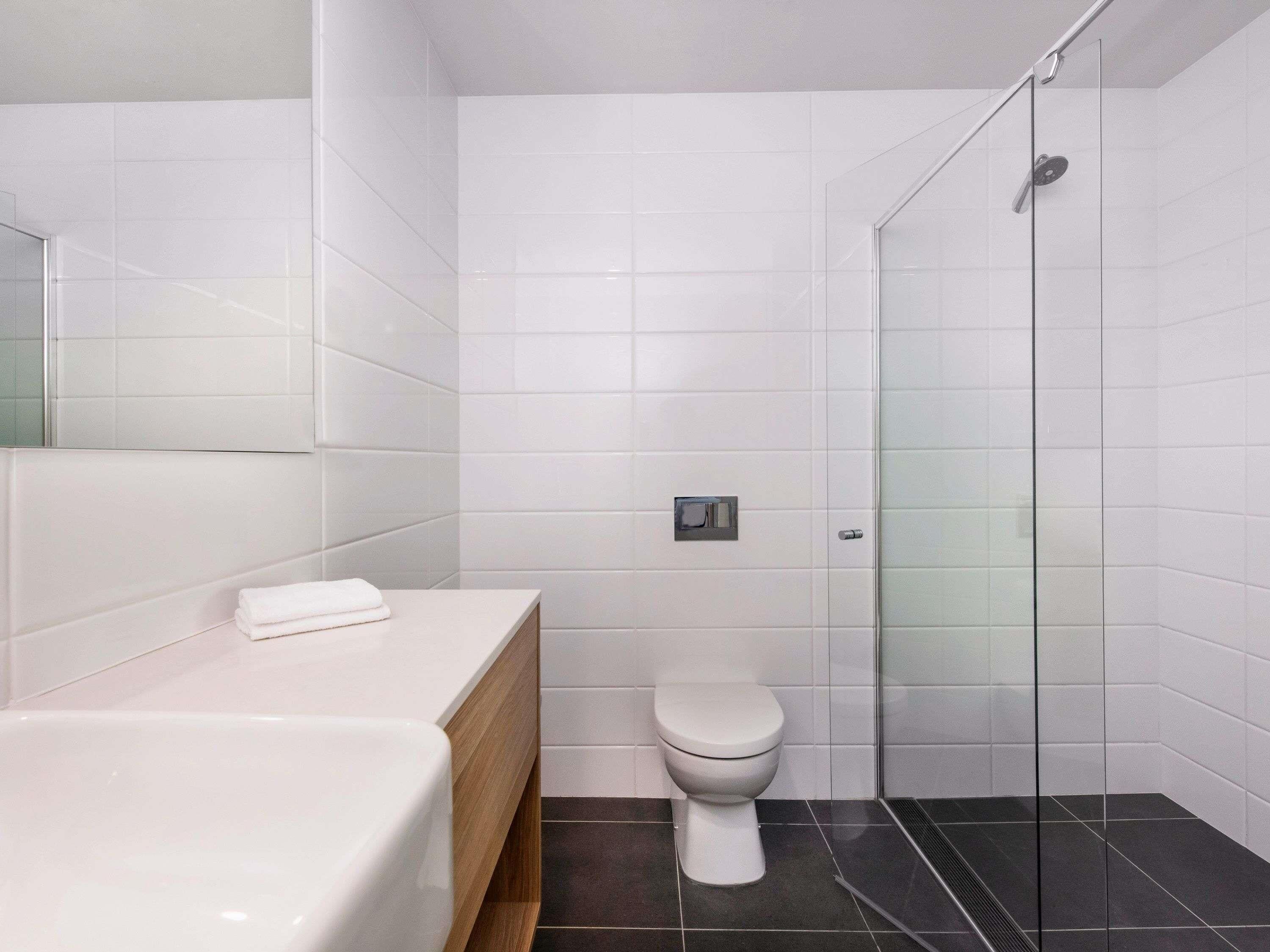 A modern bathroom with a white toilet, a glass shower enclosure, and a white sink with a wooden countertop.