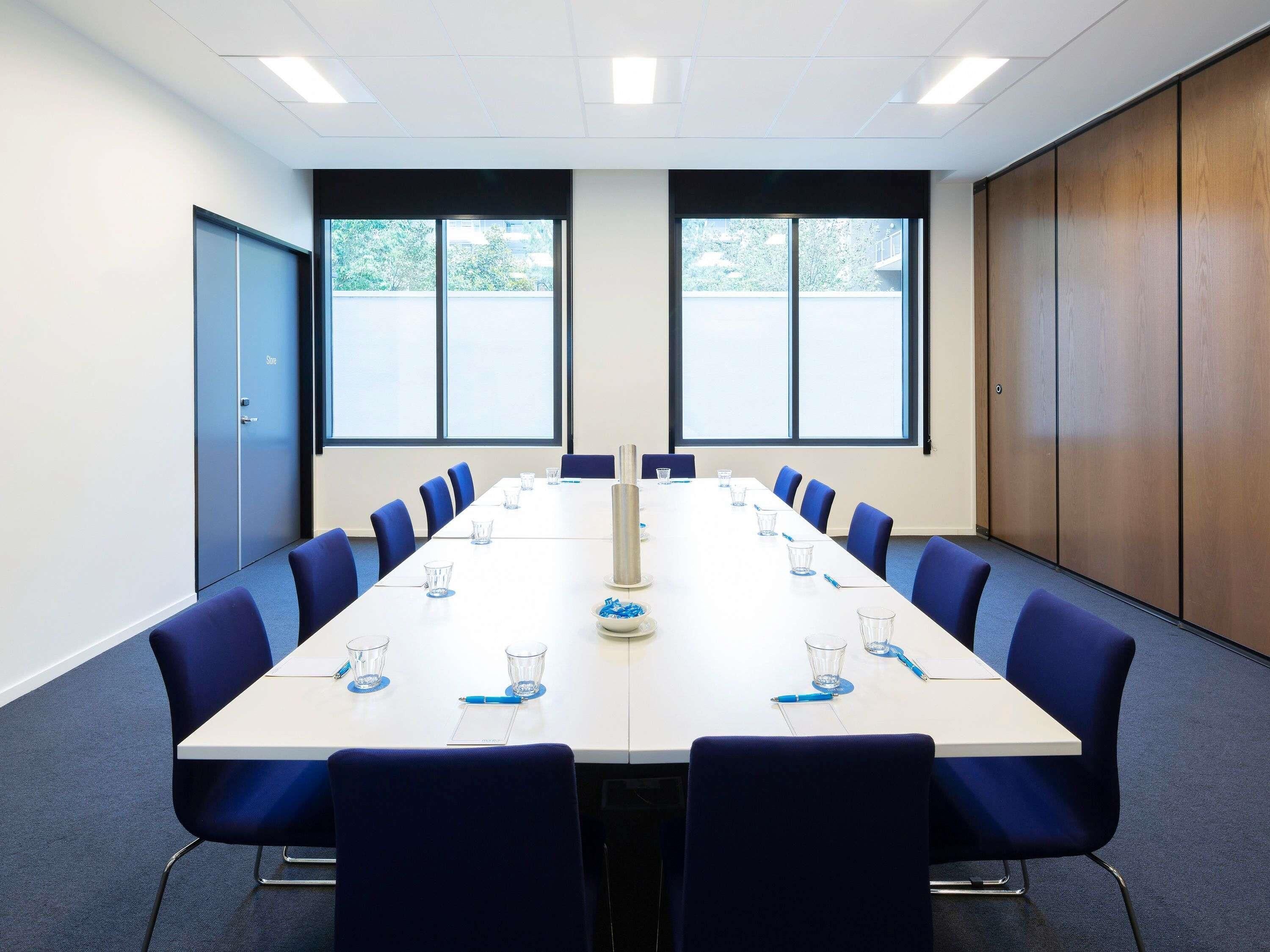 A conference room with a long table, blue chairs, and large windows.