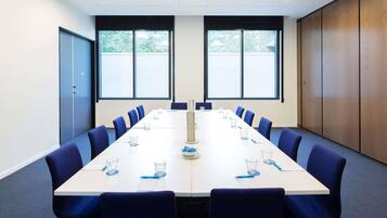 A conference room with a long table, blue chairs, and large windows.