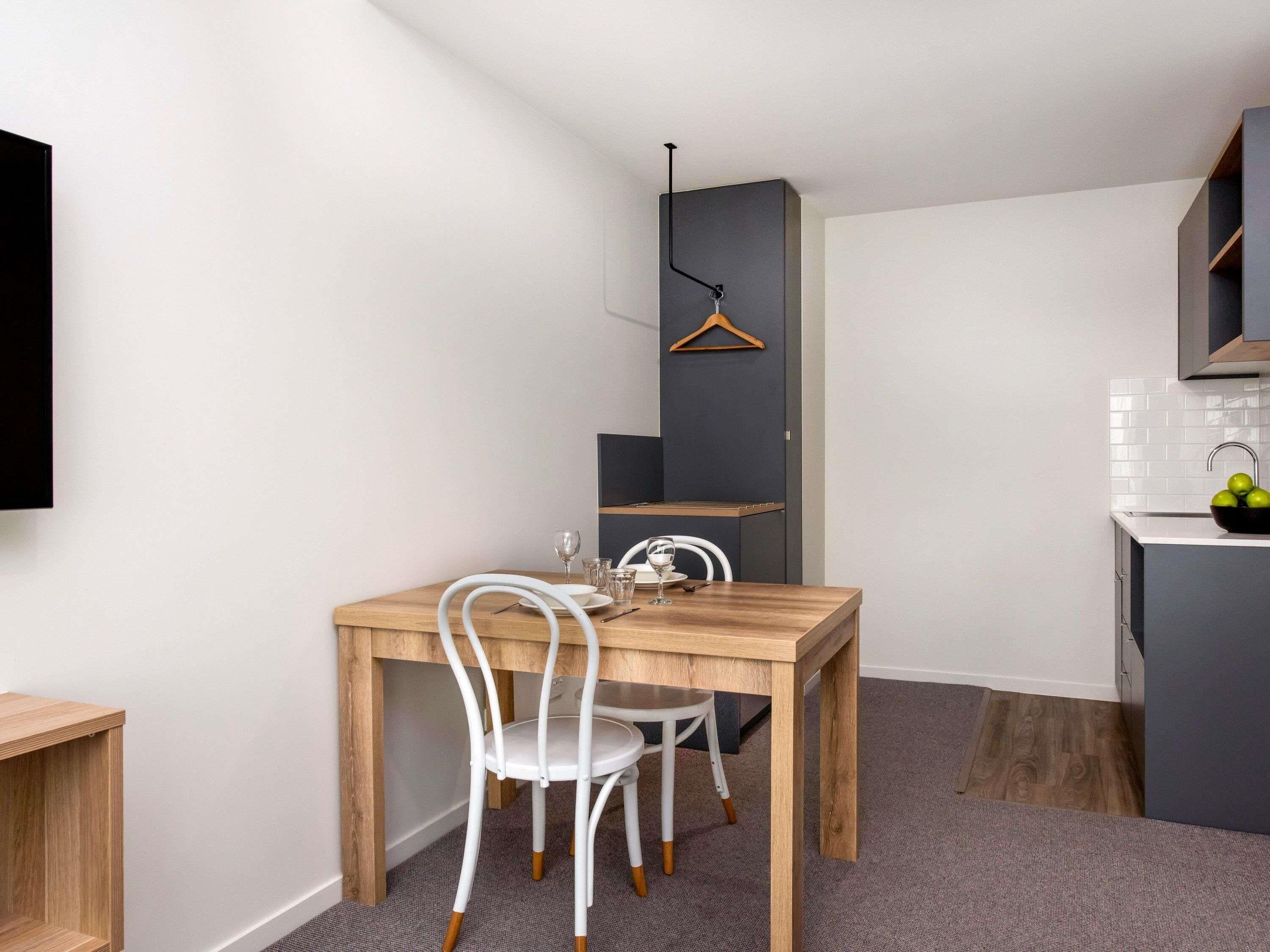 Una cocina moderna con una mesa y sillas de madera, una lámpara colgante y un lavamanos pequeño con manzanas.