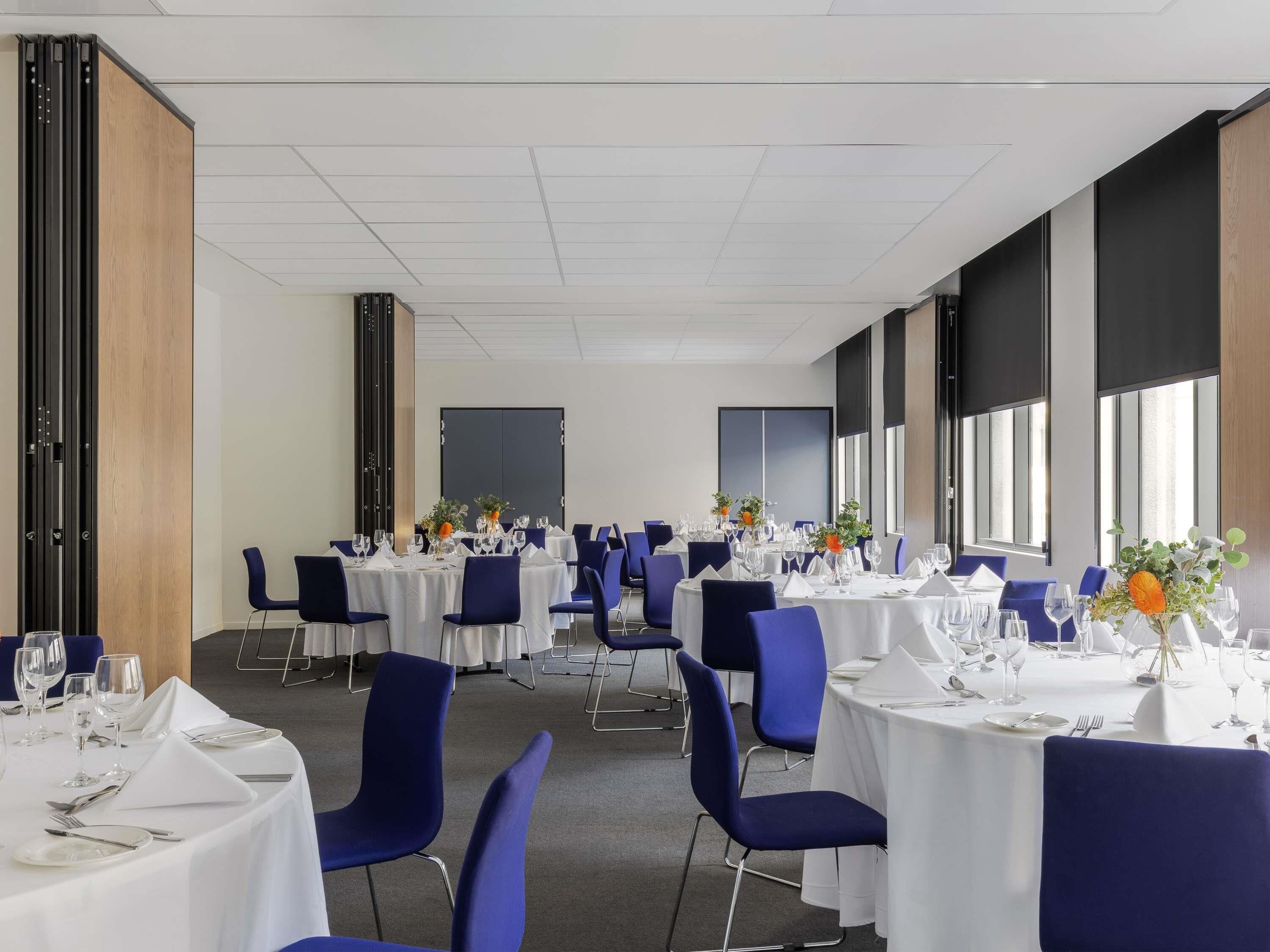 A conference room with multiple tables, blue chairs, and white tablecloths.