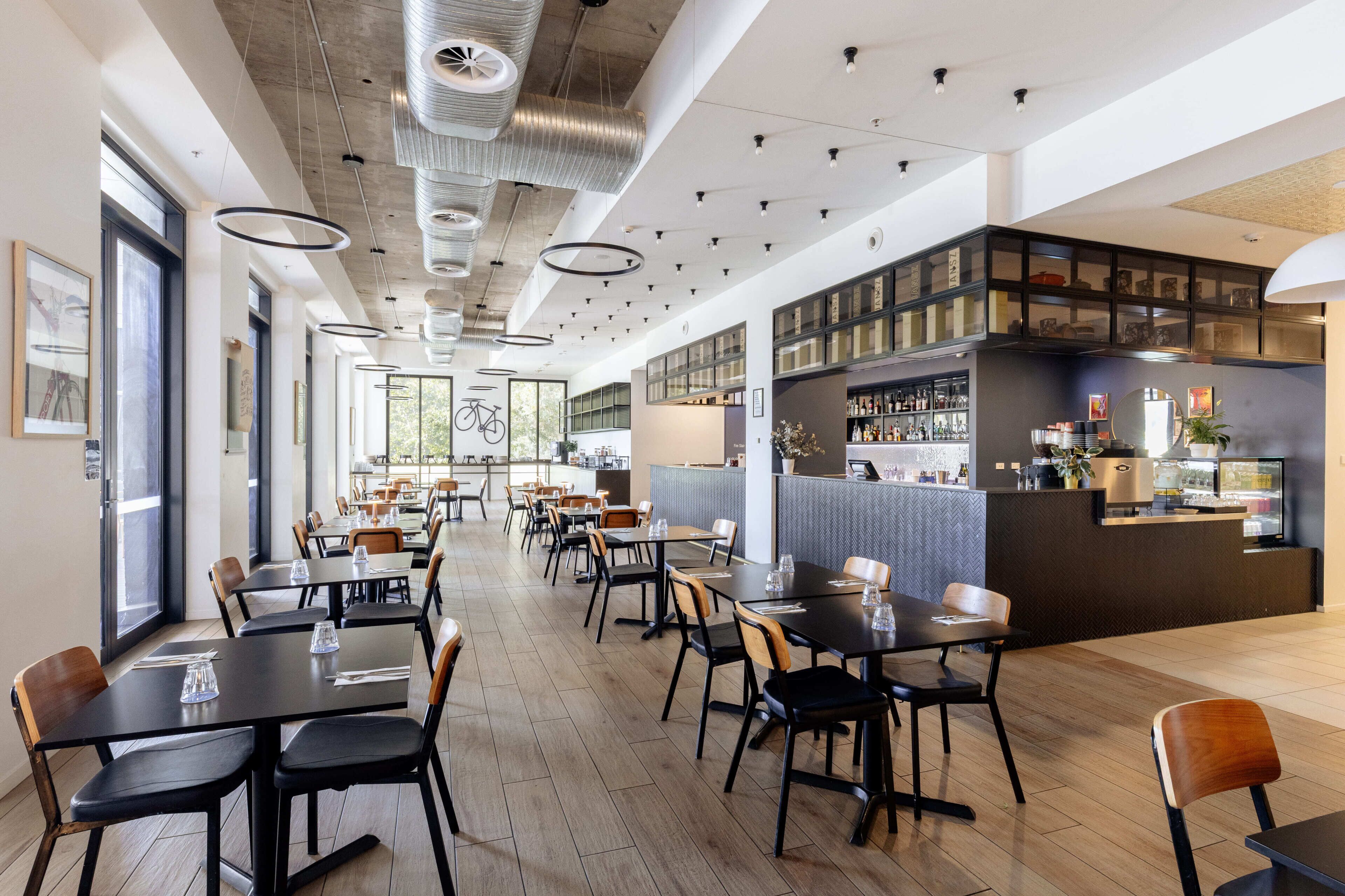 A modern restaurant with wooden flooring, black and brown chairs, and a bar area with glass display cases.