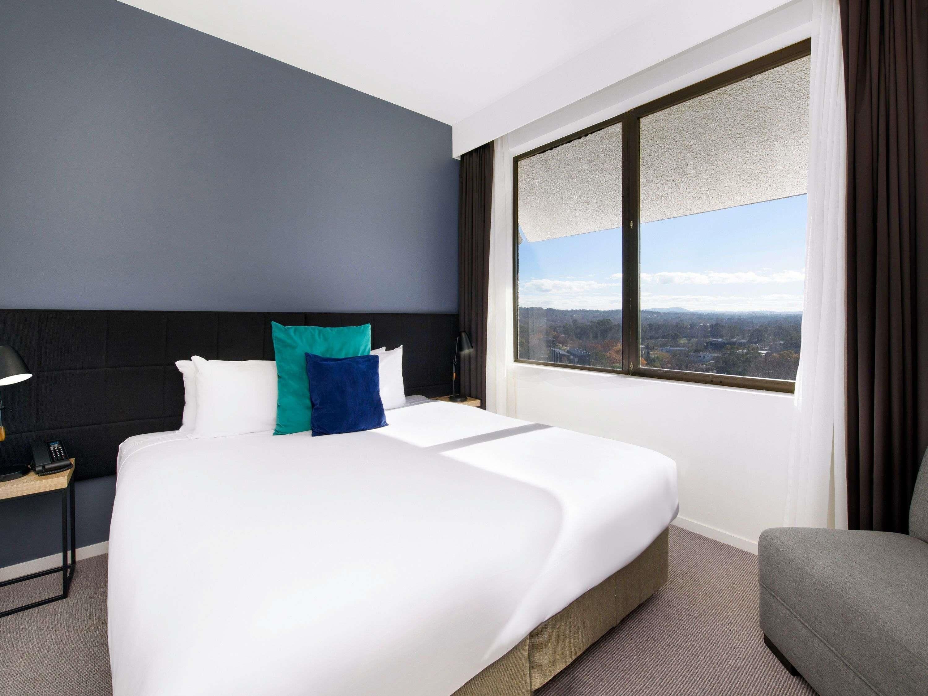 Una habitación de hotel con una cama, un escritorio, una silla y un ventanal con vistas.
