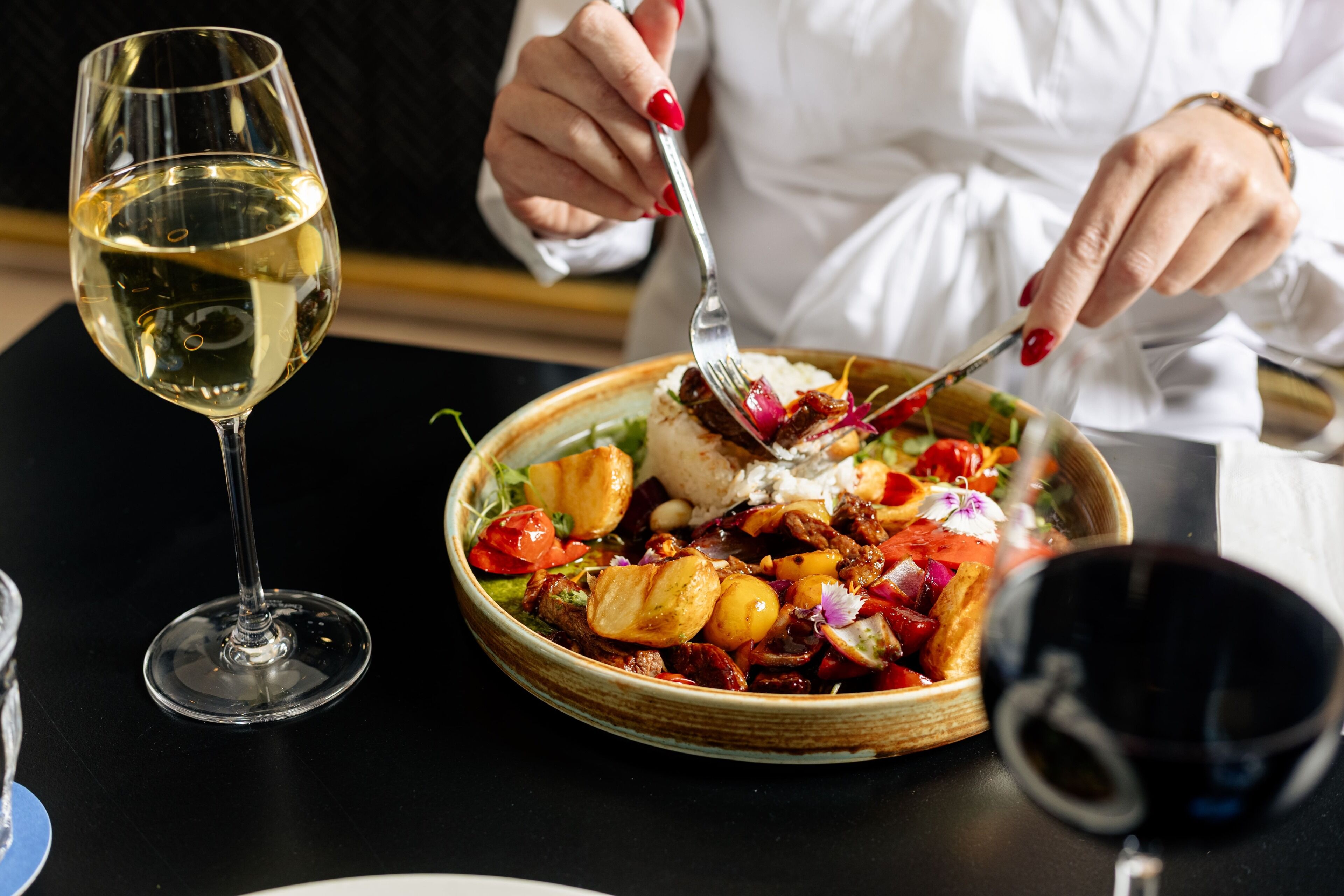 Une table à manger avec une assiette de nourriture, un verre de vin blanc et un verre de vin rouge.
