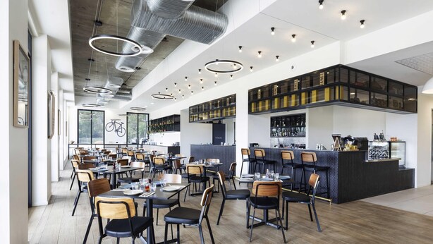 Un interior de restaurante moderno con techos altos, conductos expuestos y una zona de bar.