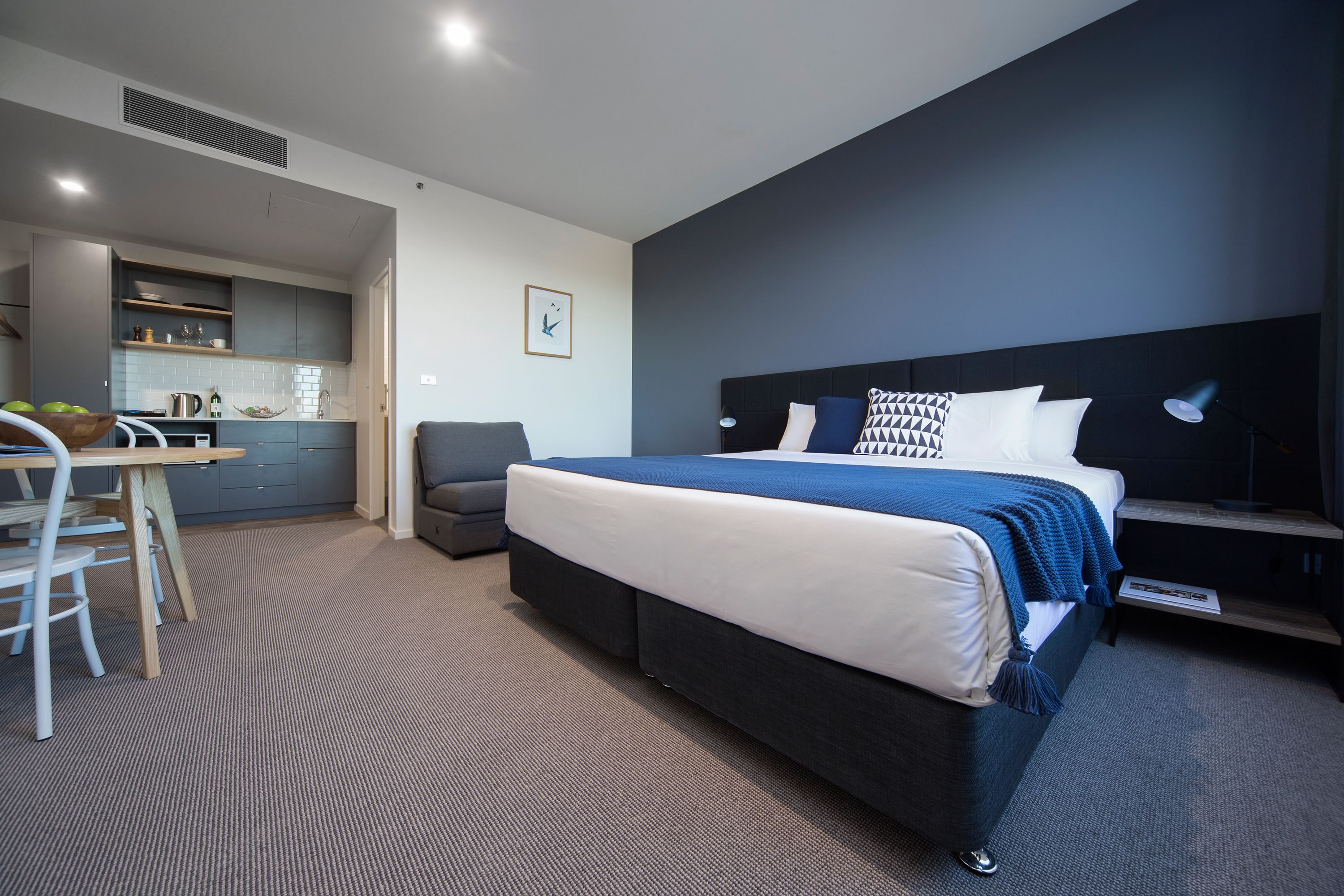 Quarto de hotel moderno com uma cama grande, uma escrivaninha e uma cozinha compacta.