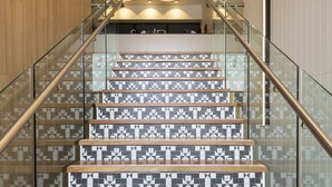 Una escalera con un diseño geométrico de azulejos y escalones de madera, que lleva a una habitación de diseño moderno con iluminación colgante.