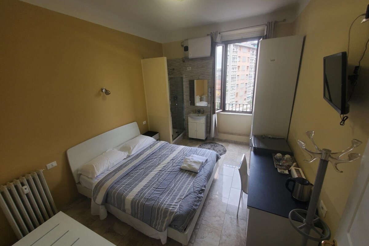 Ein Schlafzimmer mit einem Bett, einem Schreibtisch, einem Heizkörper, einem Fenster und einem Fernseher.