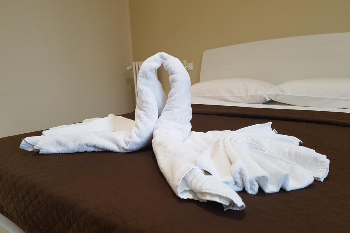 A bed with a brown cover and two towels arranged in a swan shape.
