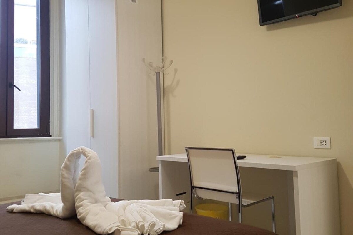 Ein Schlafzimmer mit einem Bett, einem Schreibtisch, einem Stuhl, einem Fernseher und einem Fenster.
