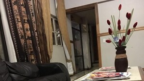 A living room with a black leather sofa, a wooden coffee table with magazines, a patterned rug, and a vase with red flowers. - Tassili Lodge (Kempton Park)