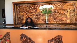 A reception desk with a large wooden carving of animals and the name 'TASSILWOOD'. - Tassili Lodge (Kempton Park)