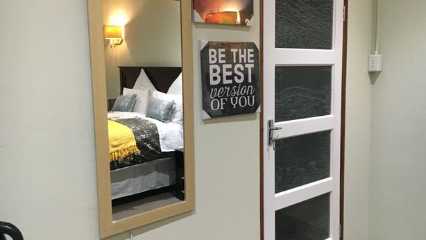 A bedroom with a bed, a mirror, a motivational sign, and a door. - Tassili Lodge (Kempton Park)
