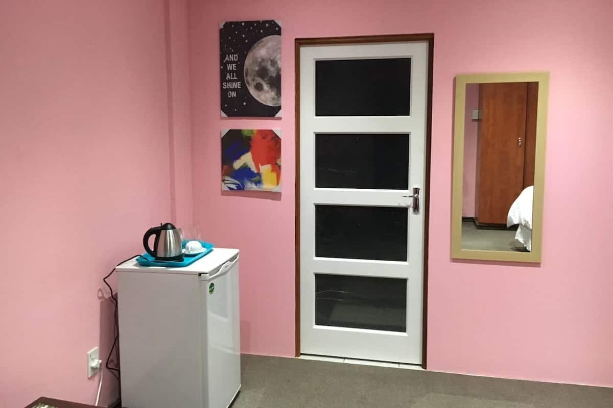 Een kamer met een roze muur, een witte deur, een kleine witte koelkast en een spiegel.