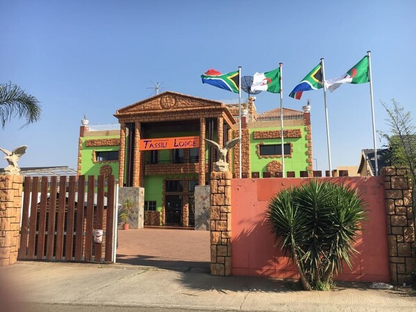 A lodge with a sign reading "TASSILI LODGE" and multiple flags in front.