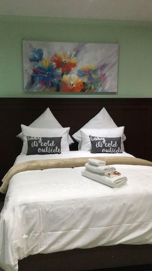 A hotel room with a bed, pillows, a blanket, and a painting on the wall.
