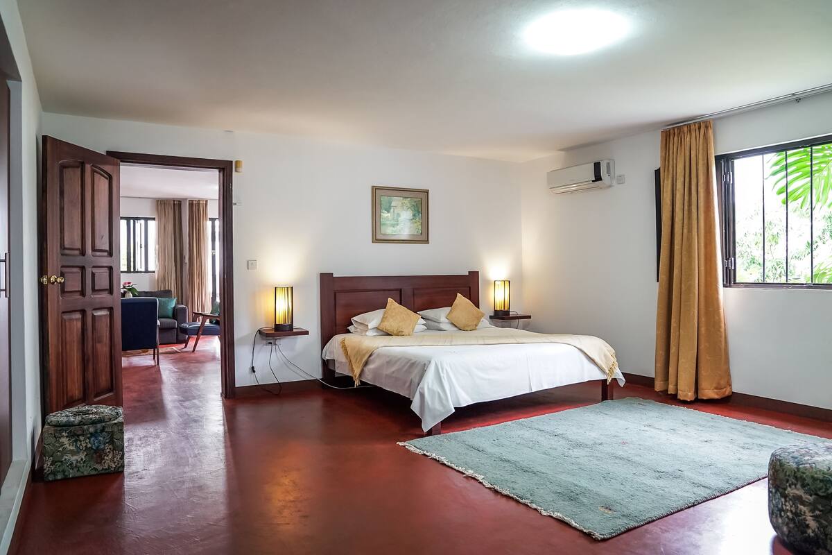 Une chambre à coucher avec un lit en bois, deux tables de chevet avec des lampes, une fenêtre avec des rideaux et une vue sur l’extérieur.