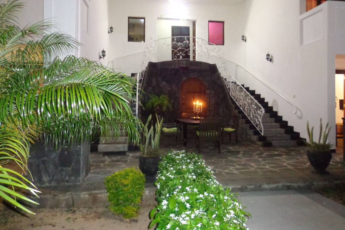 Un escalier en pierre mène à une salle à manger dotée d’une cheminée, qui est entourée de plantes en pot et d’un palmier.