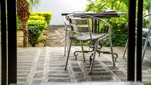 A patio area with a metal chair and table, surrounded by greenery and a stone pathway. - Royal Ho (Grand-Baie)