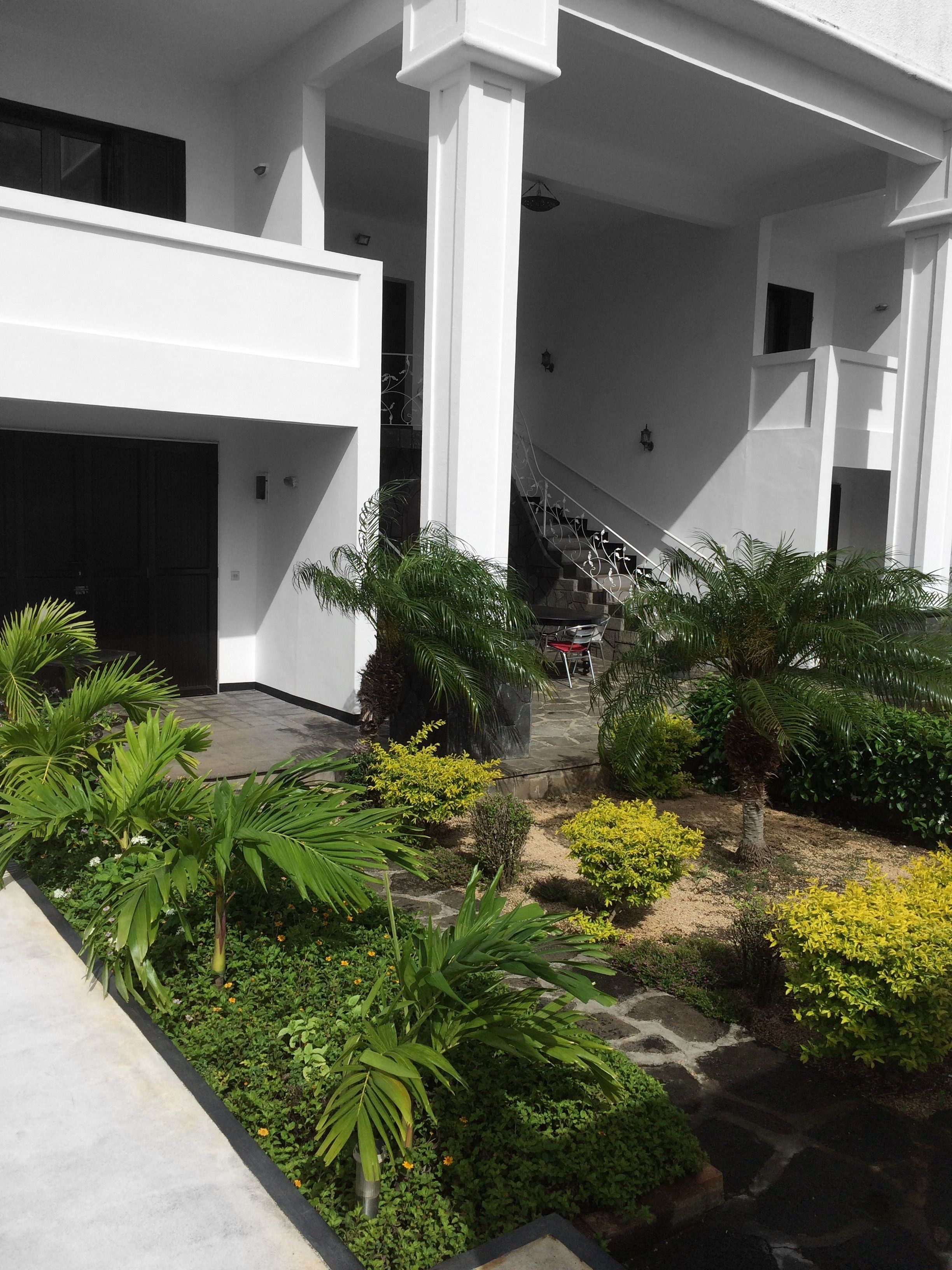A modern building with a covered outdoor area featuring a staircase, potted plants, and a stone pathway.