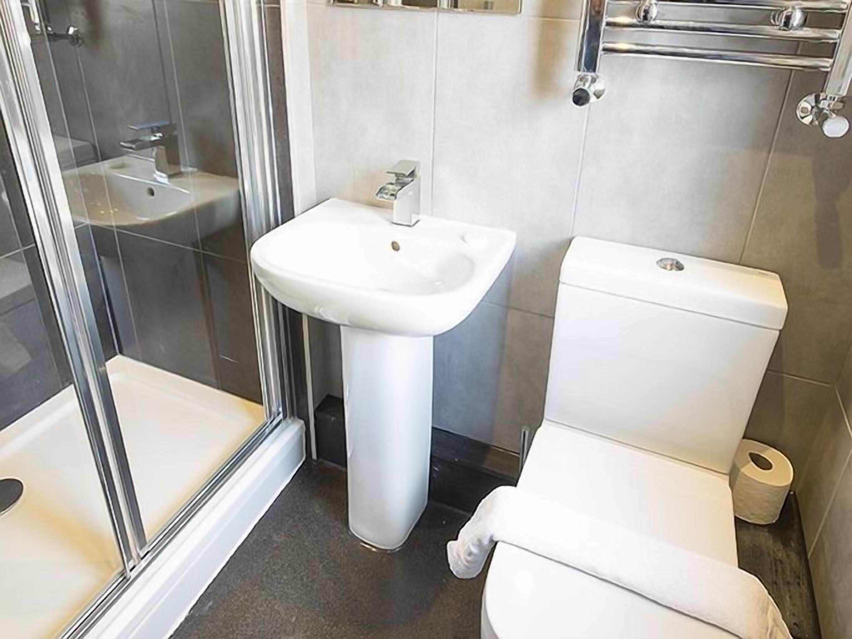 Ein Badezimmer mit Duschkabine aus Glas, einem Standwaschbecken und einer Toilette.