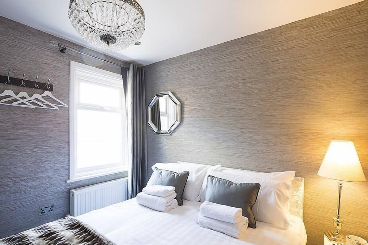 A modern hotel room with a large bed, a chandelier, a mirror, and a bedside lamp.