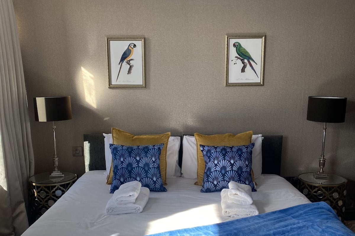 A hotel room with a large bed, two framed bird paintings on the wall, and two nightstands with lamps.