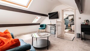 A modern living room with a sofa, a round coffee table, and a teal armchair. A TV is mounted on the wall, and a skylight is visible. - Arthur's of Churchtown (Southport)