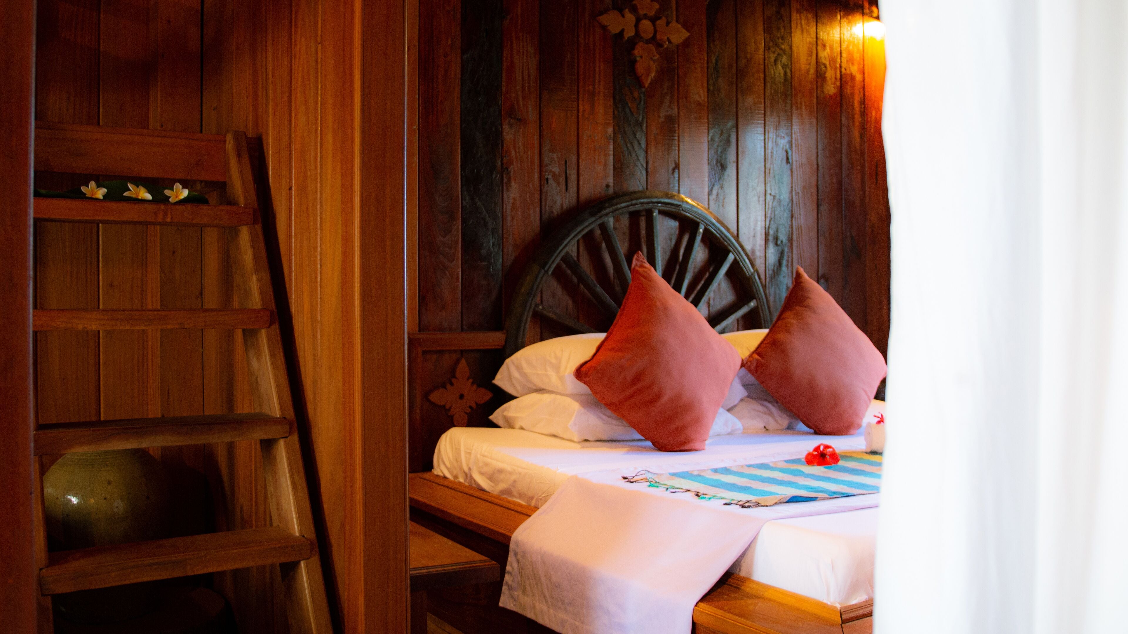 A wooden bed with white and red pillows, a striped blanket, and a vase on the nightstand.