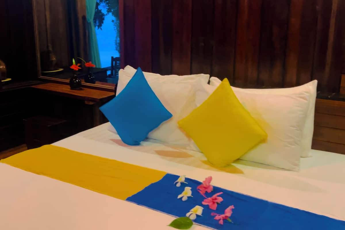 A neatly made bed with a blue and yellow bedspread, white pillows, and a blue and yellow pillow on the headboard.