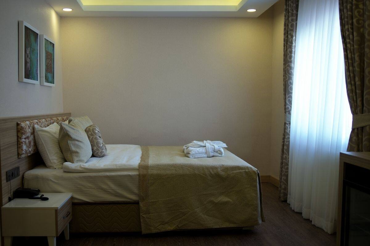 A neatly made bed with a headboard, a bedside table with a lamp, and a window with curtains.