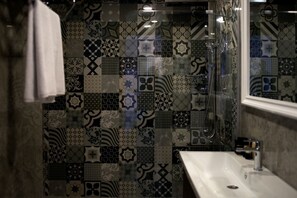 Un baño con lavabo, espejo y ducha. Las paredes están revestidas con distintos diseños.