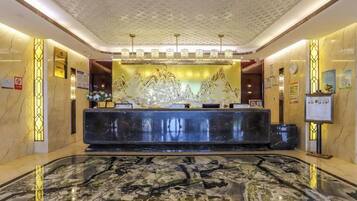 A hotel reception area with a marble floor, a reception desk, and a decorative wall.