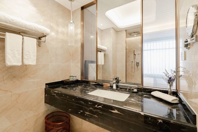 A modern bathroom with a black marble countertop, a large mirror, and a glass shower enclosure.