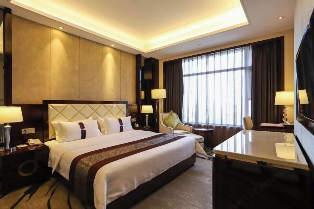 Ein Hotelzimmer mit einem großen Bett, Nachttischen, einem Schreibtisch und einem Fernseher.