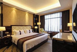 Ein Hotelzimmer mit einem großen Bett, Nachttischen, einem Schreibtisch und einem Fernseher.