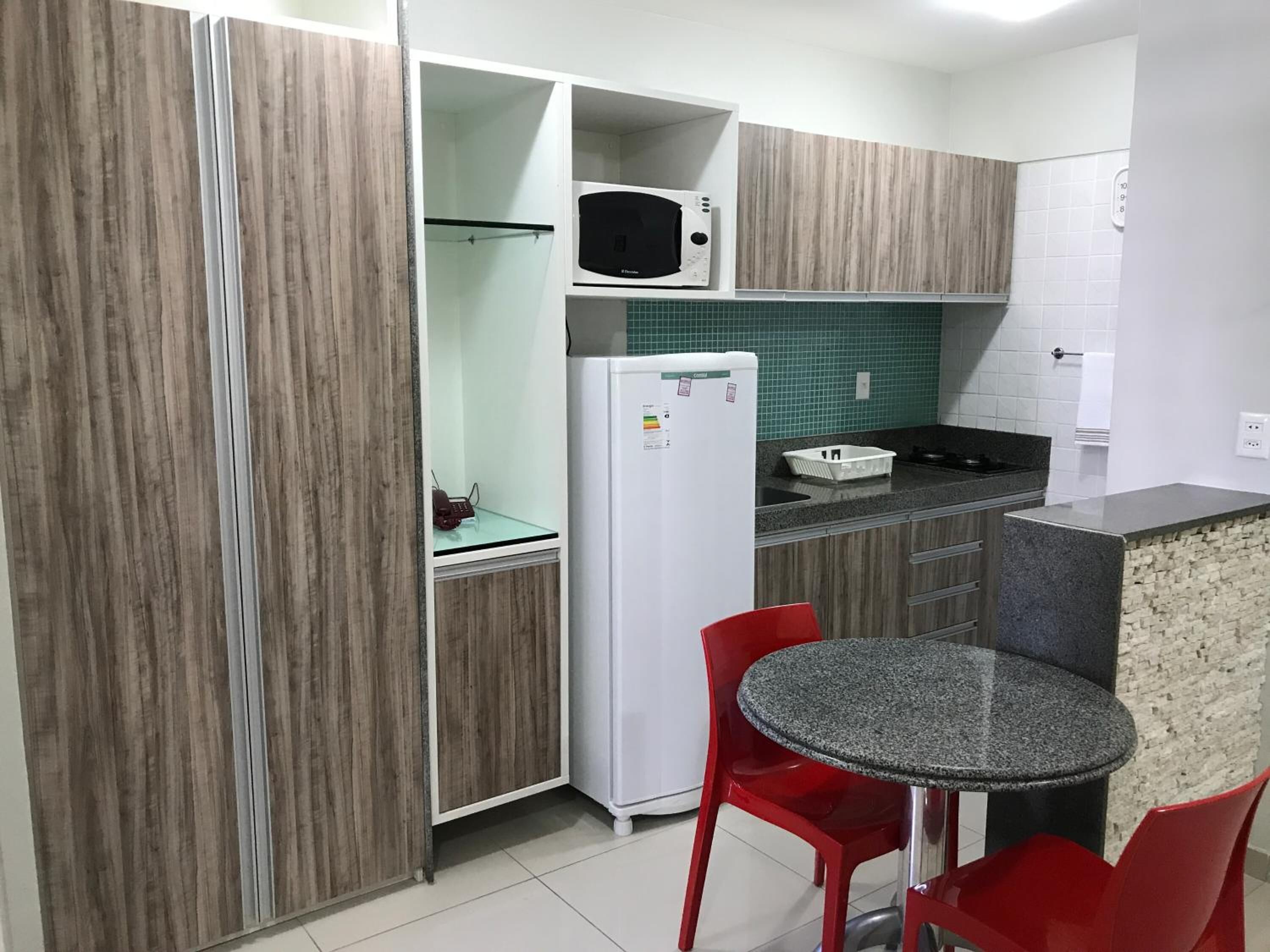 Une cuisine compacte équipée d’un four à micro-ondes, d’un réfrigérateur et d’un petit coin repas avec des chaises rouges.