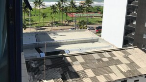 Une vue depuis une fenêtre donnant sur une plage bordée de palmiers et sur un bâtiment dont le toit est fait de tôles ondulées.