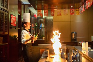 A chef performing a flambé with a bottle in a kitchen setting.