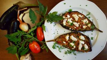 Dos berenjenas rellenas en un plato con guarnición de perejil, rodeadas de verduras frescas como tomates y ajo.